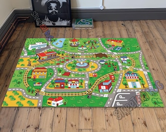May include: A rectangular play rug with a town map design. The rug features roads, buildings, a train track, and a park with a carousel and fountain. The color palette includes green, yellow, gray, red, and white.