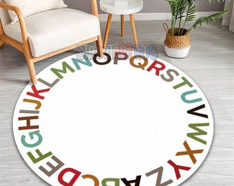 May include: A white, round rug with the alphabet in various colors arranged around the edge. The letters are in a sans-serif font. The rug is on a light-colored wooden floor, with a chair and side table in the background.