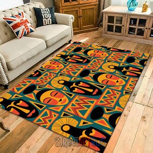 May include: A rectangular rug with a striking African tribal mask design. The rug has a teal background with repeating orange, yellow, and black mask designs and geometric shapes. The rug is on a wooden floor.