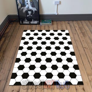 May include: A rectangular rug with a soccer ball pattern. The rug features a repeating design of black and white hexagons, creating a classic soccer ball appearance. The rug is placed on a wooden floor.