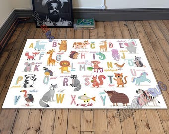May include: A rectangular white rug featuring the alphabet with colorful illustrations of animals. Each letter has a corresponding animal, such as a giraffe for G and a zebra for Z. The rug is on a wooden floor.