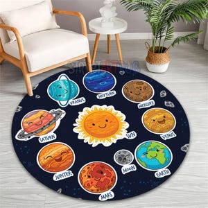 May include: A round, navy blue rug featuring a cartoon illustration of the solar system. The rug includes the sun and planets like Earth, Saturn, and Jupiter, each with a smiling face. The planets are labeled with their names in white text.