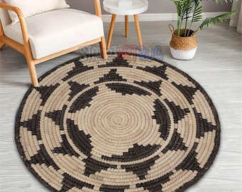 May include: A round woven rug with a geometric pattern in shades of brown and beige. The rug has a dark brown border and a central spiral design. This decorative rug is suitable for living rooms and bedrooms.