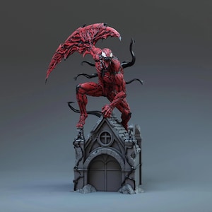 May include: A red and black Carnage statue, a Marvel Comics character, is posed atop a gray miniature church. The figure has a detailed muscular physique, with black tendrils and a large wing-like structure. The statue is a collectible item.