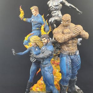 Op de afbeelding: Een gedetailleerd beeldje van de Fantastic Four en Silver Surfer. De figuren staan in dynamische poses, met de Human Torch in vlammen. The Thing is rotsachtig oranje van kleur en de Silver Surfer is metallic zilver. Het team draagt blauwe en zwarte pakken.