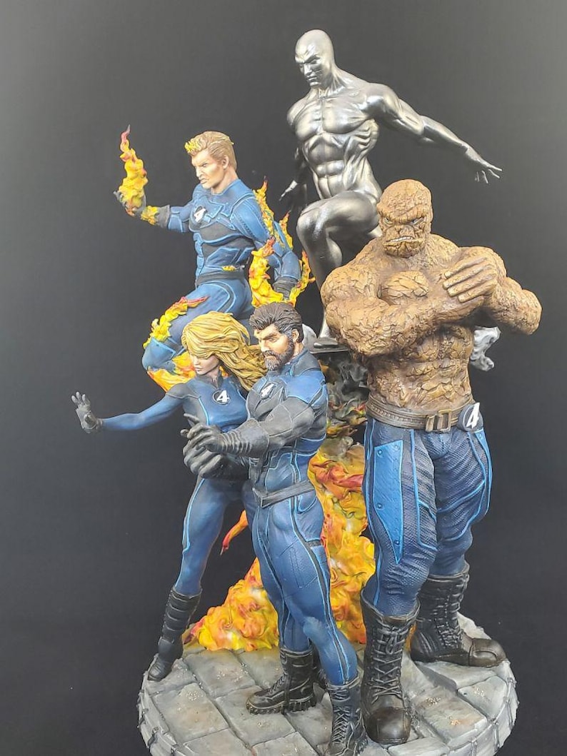 Op de afbeelding: Een gedetailleerd beeldje van de Fantastic Four en Silver Surfer. De figuren staan in dynamische poses, met de Human Torch in vlammen. The Thing is rotsachtig oranje van kleur en de Silver Surfer is metallic zilver. Het team draagt blauwe en zwarte pakken.