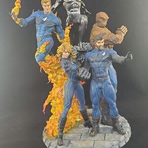 Op de afbeelding: Een gedetailleerd beeldje van de Fantastic Four en Silver Surfer. De figuren staan in dynamische poses, met levendige kleuren en ingewikkelde details. De basis is een steenachtig platform.