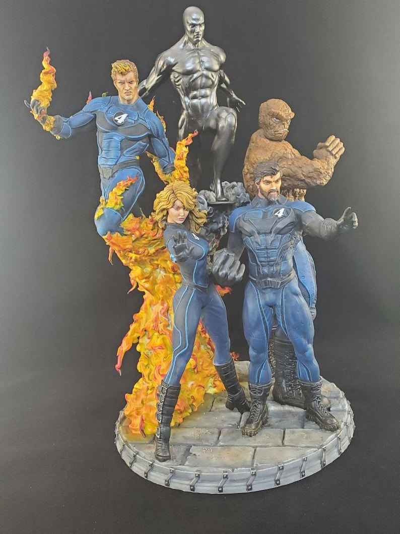 Op de afbeelding: Een gedetailleerd beeldje van de Fantastic Four en Silver Surfer. De figuren staan in dynamische poses, met levendige kleuren en ingewikkelde details. De basis is een steenachtig platform.