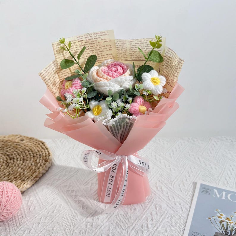 Puede incluir: Un ramo de flores de ganchillo hechas a mano en tonos rosa, blanco y amarillo, envuelto en papel rosa y p&aacute;ginas de libros antiguos. El ramo est&aacute; atado con una cinta blanca que dice "JUST FOR YOU".