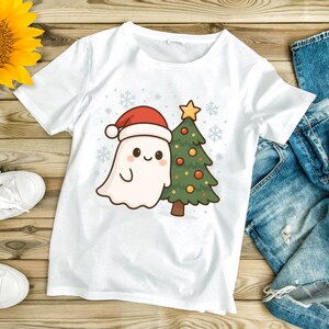 May include: White t-shirt with a cartoon ghost wearing a Santa hat and a Christmas tree. The ghost has a smiling face and the tree is decorated with baubles and a star. Snowflakes are in the background.