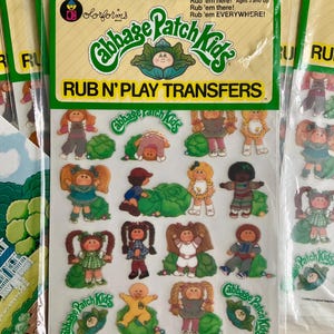 Puede incluir: Una hoja de calcomanías Cabbage Patch Kids Rub N' Play con varias pegatinas de personajes de dibujos animados y gráficos de repollos verdes. El empaque incluye el texto Rub 'em here! Rub 'em there! Rub 'em EVERYWHERE! y Cabbage Patch Kids.
