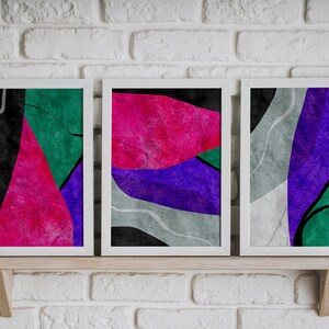 May include: Three framed abstract art prints with a modern, geometric design. The prints feature a mix of pink, purple, green, black, and gray colors.