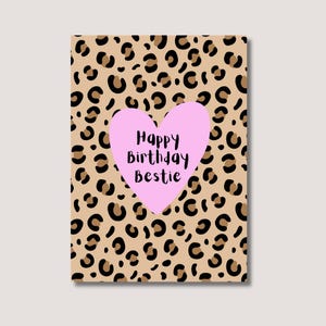 Könnte beinhalten: Rechteckige Grußkarte mit beigem Leopardenmuster. Ein rosa Herz in der Mitte trägt den schwarzen Schriftzug "Happy Birthday Bestie". Die Karte hat einen weißen Rand.