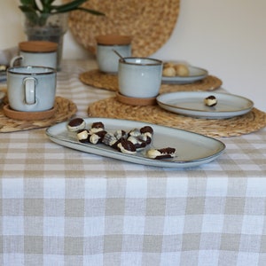 May include: A white and brown gingham tablecloth with a white oval serving dish filled with chocolate covered sweets. The sweets are arranged in a cluster on the dish. The dish is sitting on top of the tablecloth.
