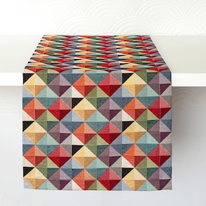 Peut inclure: Un chemin de table rectangulaire présentant un motif géométrique répétitif de losanges et de triangles dans une palette vibrante de rouge, orange, jaune, vert, bleu et violet. Le tissu tissé affiche un design à grille texturée.