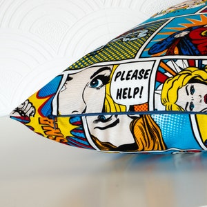 Può includere: Un cuscino colorato con un design a fumetti che presenta una donna con i capelli biondi e le parole "PLEASE HELP!" in un fumetto.