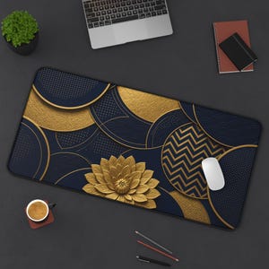 May include: A rectangular desk mat featuring a dark navy blue and gold geometric pattern with overlapping circles, chevron lines, and a central gold lotus flower design. A white computer mouse rests on the right side of the mat.