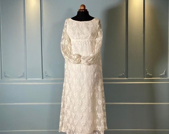 May include: A white lace wedding dress with long sleeves and a fitted bodice. The dress has a flowing skirt and is displayed on a mannequin against a blue wall.