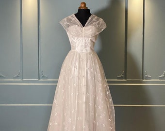 May include: A white vintage wedding dress with a tulle skirt and embroidered floral details. The dress has a fitted bodice with a V-neckline and short sleeves.