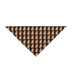 May include: A triangular bandana featuring a repeating pattern of light orange ghost figures on a solid black background. The ghosts are depicted with simple oval eyes and a rounded top, arranged in a grid across the entire fabric surface.