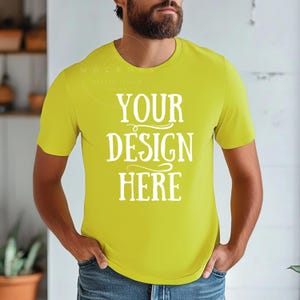 Può includere: Una maglietta gialla brillante a maniche corte e collo rotondo. La maglietta ha il testo "YOUR DESIGN HERE" stampato sul davanti in un font bianco stilizzato.