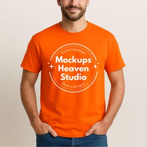 Puede incluir: Una camiseta naranja brillante con cuello redondo. La camiseta presenta un logotipo circular blanco con el texto "Mockups Heaven Studio" y las frases "Perfect mockups" y "Perfect designs". La camiseta la lleva una persona.