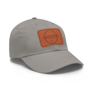 May include: A gray baseball cap with a brown leather patch featuring the text "Gaston's Tavern Est 1981".