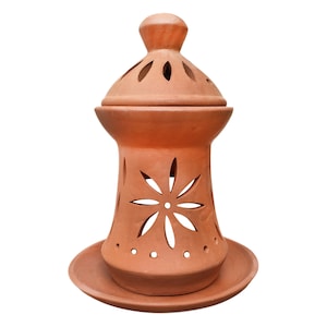 May include: A terracotta candle holder with a decorative flower design and a removable lid. The holder has a wide base and a narrow top, with a small opening at the top for the candle.