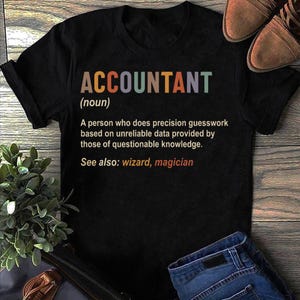 Op de afbeelding: Zwart T-shirt met een humoristische definitie van een accountant. De tekst luidt "ACCOUNTANT (zelfstandig naamwoord) Een persoon die nauwkeurige schattingen maakt op basis van onbetrouwbare gegevens die worden verstrekt door mensen met twijfelachtige kennis. Zie ook: tovenaar, magiër"