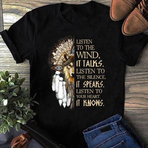 Puede incluir: Camiseta negra con un lobo y un tocado nativo americano. La camiseta incluye el texto: "Escucha al viento, habla. Escucha el silencio, habla. Escucha a tu corazón, sabe."