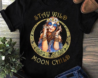 May include: Black t-shirt with a gold graphic of a woman with long brown hair wearing a flower crown and sunglasses. The text "Stay Wild Moon Child" is written in gold letters.