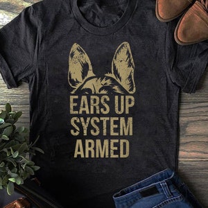 Może przedstawiać: Czarny T-shirt z przetartym obrazem uszu owczarka niemieckiego i tekstem "EARS UP SYSTEM ARMED" w kolorze złotym.