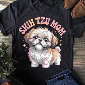 May include: Dark gray t-shirt featuring a cartoon Shih Tzu dog with the text "Shih Tzu Mom" in a pink and orange gradient. The dog is depicted with brown and white fur, and pink accents. The design includes small star details.