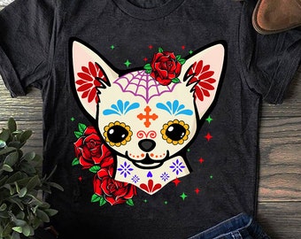 May include: A black t-shirt with a white chihuahua wearing a sugar skull design with red, orange, yellow, blue, and purple flowers. The chihuahua has black eyes and a pink nose.