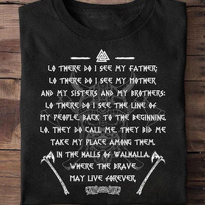 Może przedstawiać: Czarna koszulka z białym tekstem, w tym frazą „Lo there do I see my father”. Projekt zawiera wizerunki wikingów, w tym hełm, topory i ozdobny emblemat. Tematem koszulki jest mitologia nordycka.