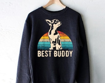 Puede incluir: Una sudadera gris oscuro con un gráfico de estilo vintage de un chihuahua sentado frente a una puesta de sol. El texto "BEST BUDDY" está impreso debajo del gráfico.