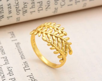 May include: A gold-toned ring featuring a delicate, openwork leaf or fern branch design that wraps around the band. The metal surface has a textured finish, and the inner band is clearly stamped with the hallmark 925, indicating sterling silver.