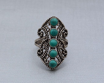 May include: An elongated silver ring featuring five round, cabochon-cut turquoise stones arranged in a vertical row. The metal band displays an intricate, textured filigree pattern with small bead-like details surrounding the central stones.