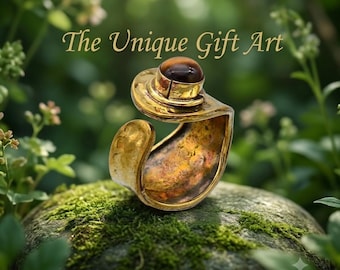 May include: A gold-toned open-ended ring featuring a smooth, dark brown, spherical gemstone set at the top. The metal band has a textured, hammered finish with a wide, curved shape. The text "The Unique Gift Art" is visible above the ring.