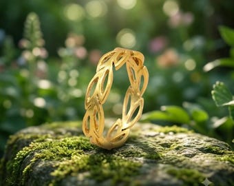 May include: A gold-toned ring featuring a continuous band of interconnected leaf-shaped cutouts. The ring is positioned upright on a mossy stone surface. The text "-The Unique Gift Art" is printed in white in the bottom right corner of the image.