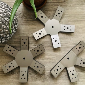 May include: Three silver metal star-shaped brackets with multiple holes. The brackets are on a wood surface.