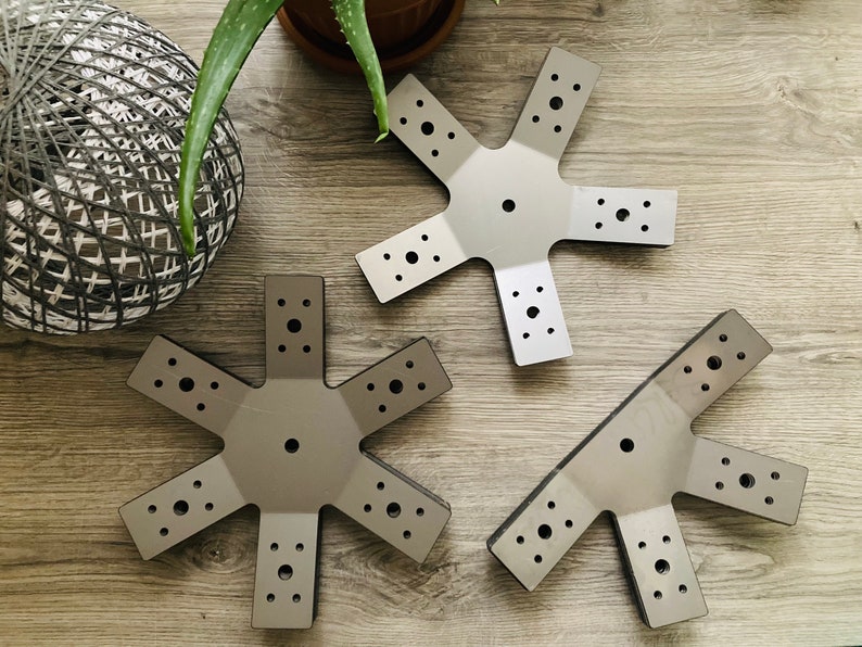 May include: Three silver metal star-shaped brackets with multiple holes. The brackets are on a wood surface.