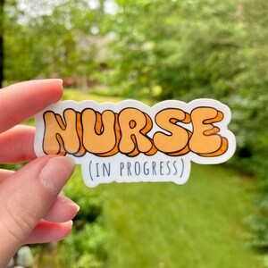 May include: A white sticker with the word "NURSE" in orange bubble letters and the text "(IN PROGRESS)" below.