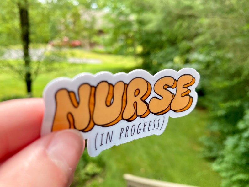 May include: A white sticker with the word "NURSE" in orange bubble letters. Below the word is the text "(IN PROGRESS)" in black.