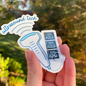 May include: A white sticker with a blue ultrasound wand and the text "ultrasound tech" above it. The wand is connected to a white cord that leads to a small white rectangle with three black and white ultrasound images of a fetus.