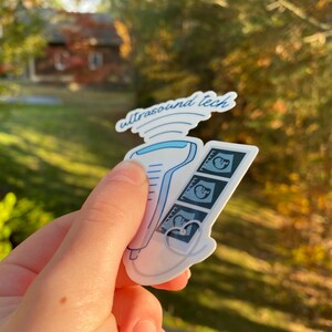 May include: A white sticker with a blue ultrasound wand and three black and white ultrasound images. The sticker says "ultrasound tech" in blue cursive writing.