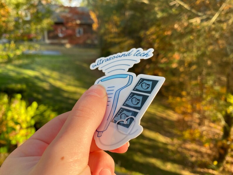 May include: A white sticker with a blue ultrasound wand and three black and white ultrasound images. The sticker says "ultrasound tech" in blue cursive writing.