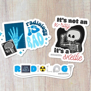 May include: Three stickers with a radiology theme. The first sticker is blue and white and says "Radiology is RAD". The second sticker is black and white and says "It's not an x-ray, it's a skeltie". The third sticker is blue and white and says "Radiology".