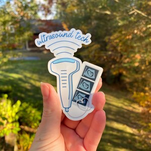 May include: A white sticker with a blue outline of an ultrasound wand and a strip of three ultrasound images. The sticker says "ultrasound tech" in blue cursive.