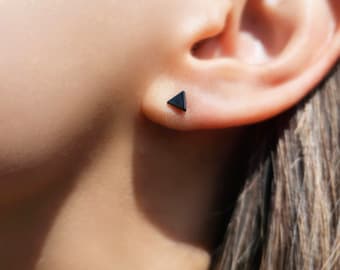 Puede incluir: Primer plano de la oreja de una persona con un pequeño pendiente triangular negro.